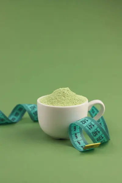 in a white cup there is a light green powder. next to a centimeter. healthy matcha tea. light green background