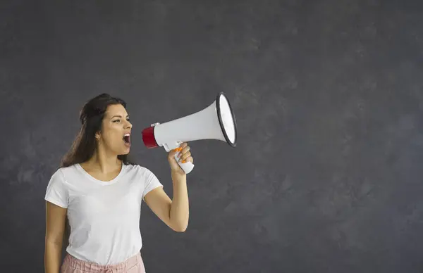 Dont miss it. Casual woman who uses a megaphone to announce advertising information or present product. Woman standing on gray background announces crazy discounts. Sale and offer concept. Copy space