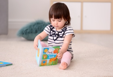 Photo of Cute baby girl with book sitting on floor at home