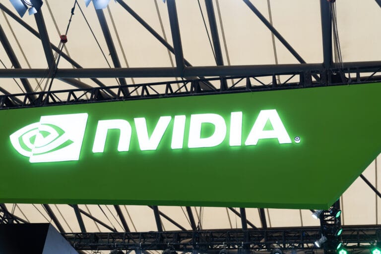 Świecące logo firmy NVIDIA na zielonym tle, zawieszone na metalowej konstrukcji z zadaszeniem.