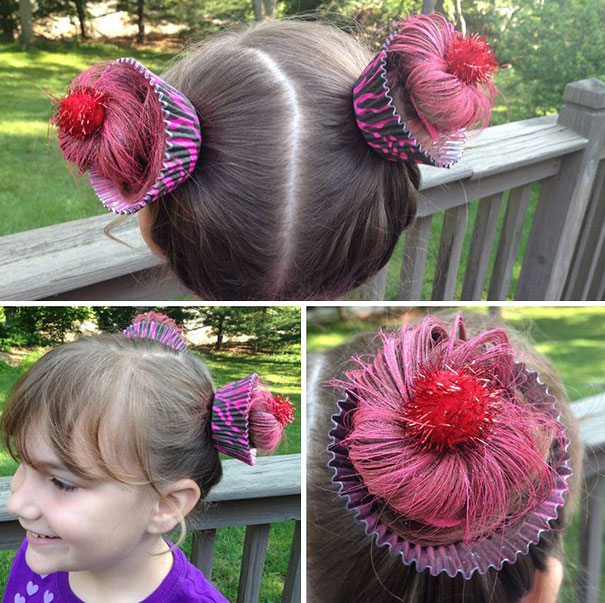 Child with a creative cupcake hairstyle, featuring pink hair buns decorated with red pom-poms on Crazy Hair Day.