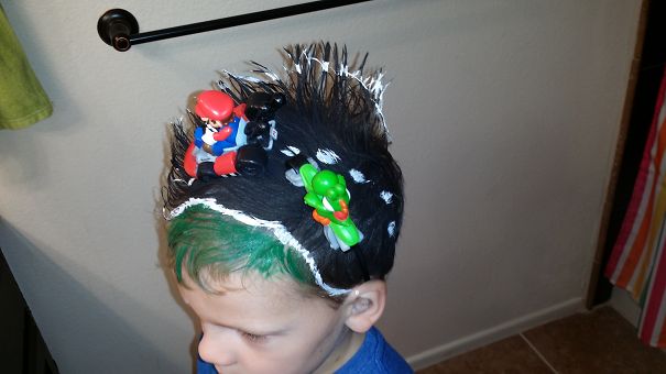 Child with a crazy hair day hairstyle featuring toy characters styled into black and green spiky hair.