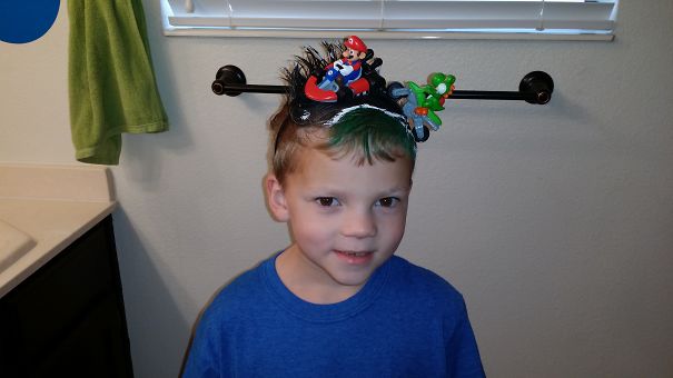 Child with a creative hairdo featuring toy figures for Crazy Hair Day, wearing a blue shirt.