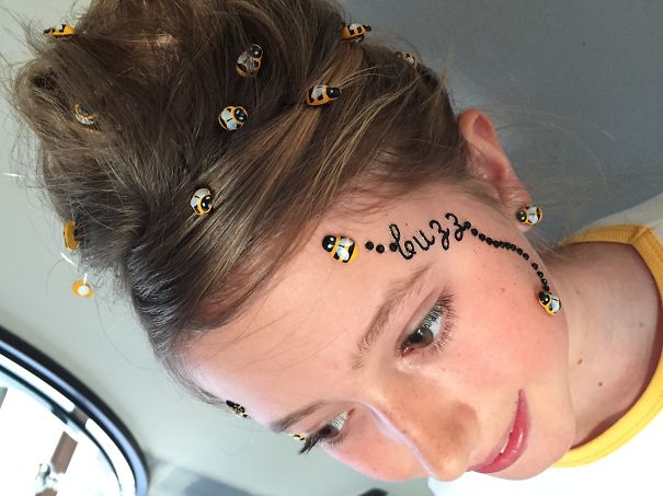 Child with bee-themed crazy hair day hairstyle, adorned with small bee ornaments and "buzz" text on the face.