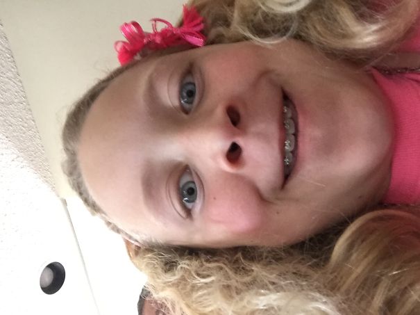 Girl with curly hair and braces smiling, featuring a pink hair accessory for a crazy hair day look.