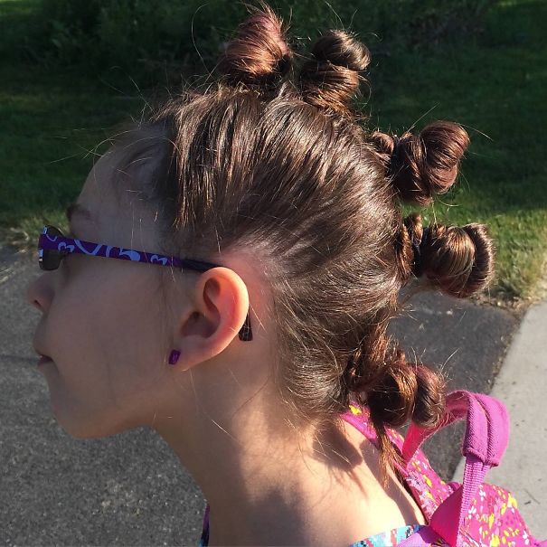 Child with creative hairstyle featuring multiple twisted buns for Crazy Hair Day, wearing purple glasses.