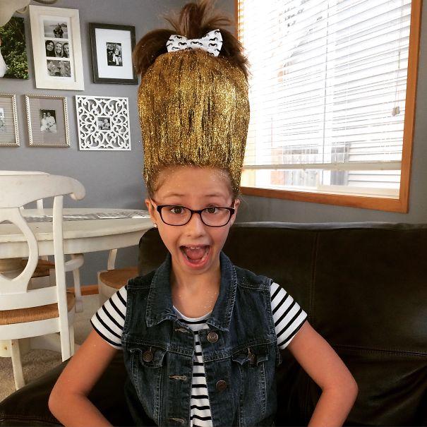 Child with a tall, gold, sparkling hairstyle and glasses on Crazy Hair Day, wearing a striped shirt and denim vest.