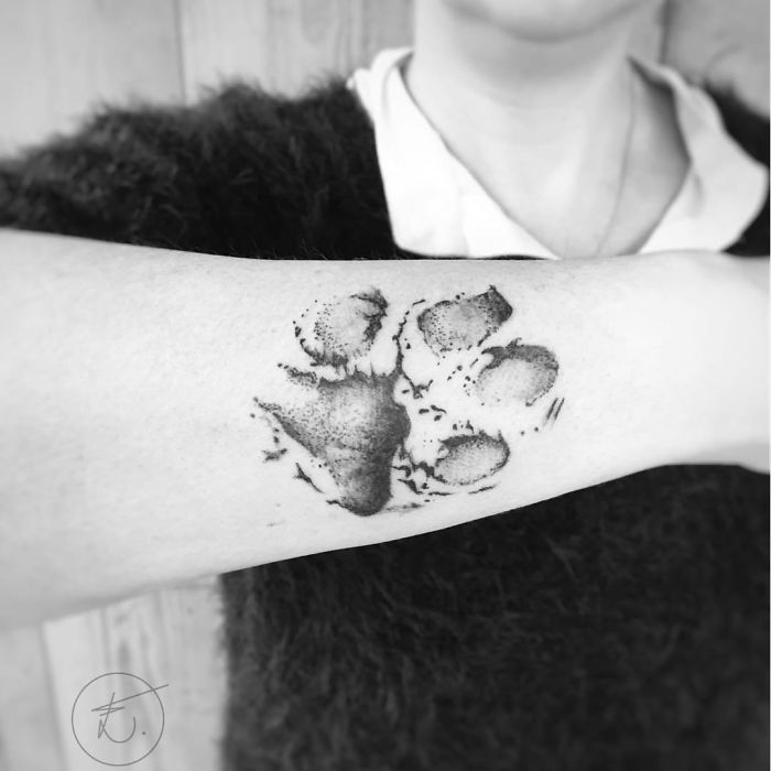 Dog paw print tattoo on forearm in black ink, showcasing a detailed and artistic design.