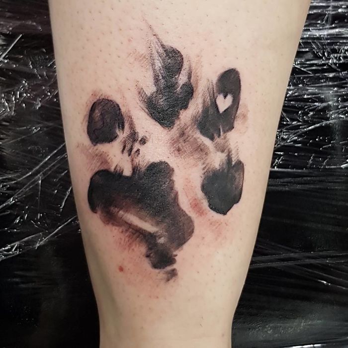 A black ink dog paw print tattoo on a person's arm, showcasing a heart shape in one pad.