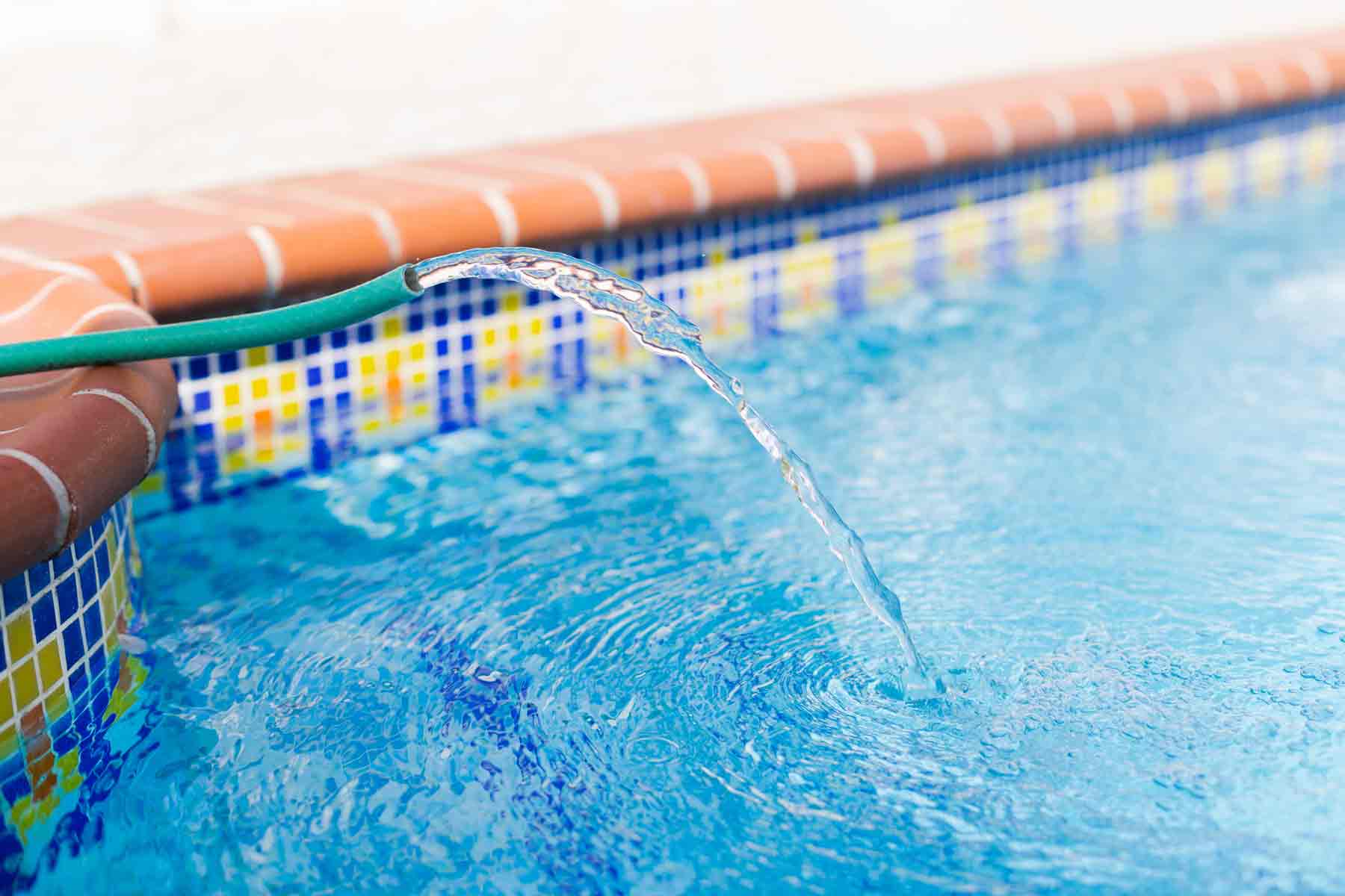 A hose filling a swimming pool with clean water.