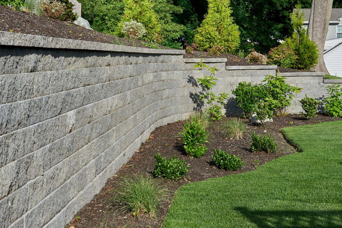 Split-face CMU cinder block retaining wall surrounding backyard landscaping