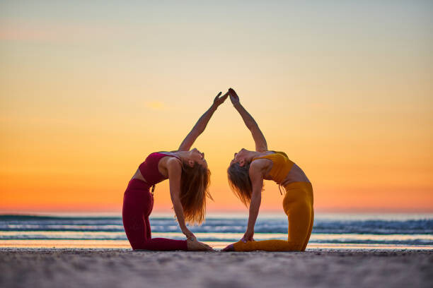 Fotografia Two women doing yoga on the beach at sunrise