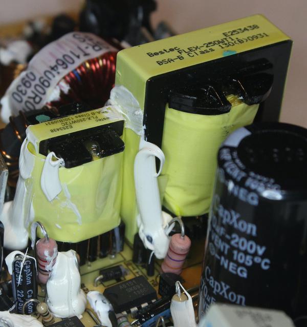 The black and yellow transformers: the transformer for standby power is on the left and the main transformer is on the right. The control IC for standby power is in front of the transformer. The large cylindrical capacitor on the right is part of the voltage doubler. The white blobs are silicone to insulate components and hold them in place.