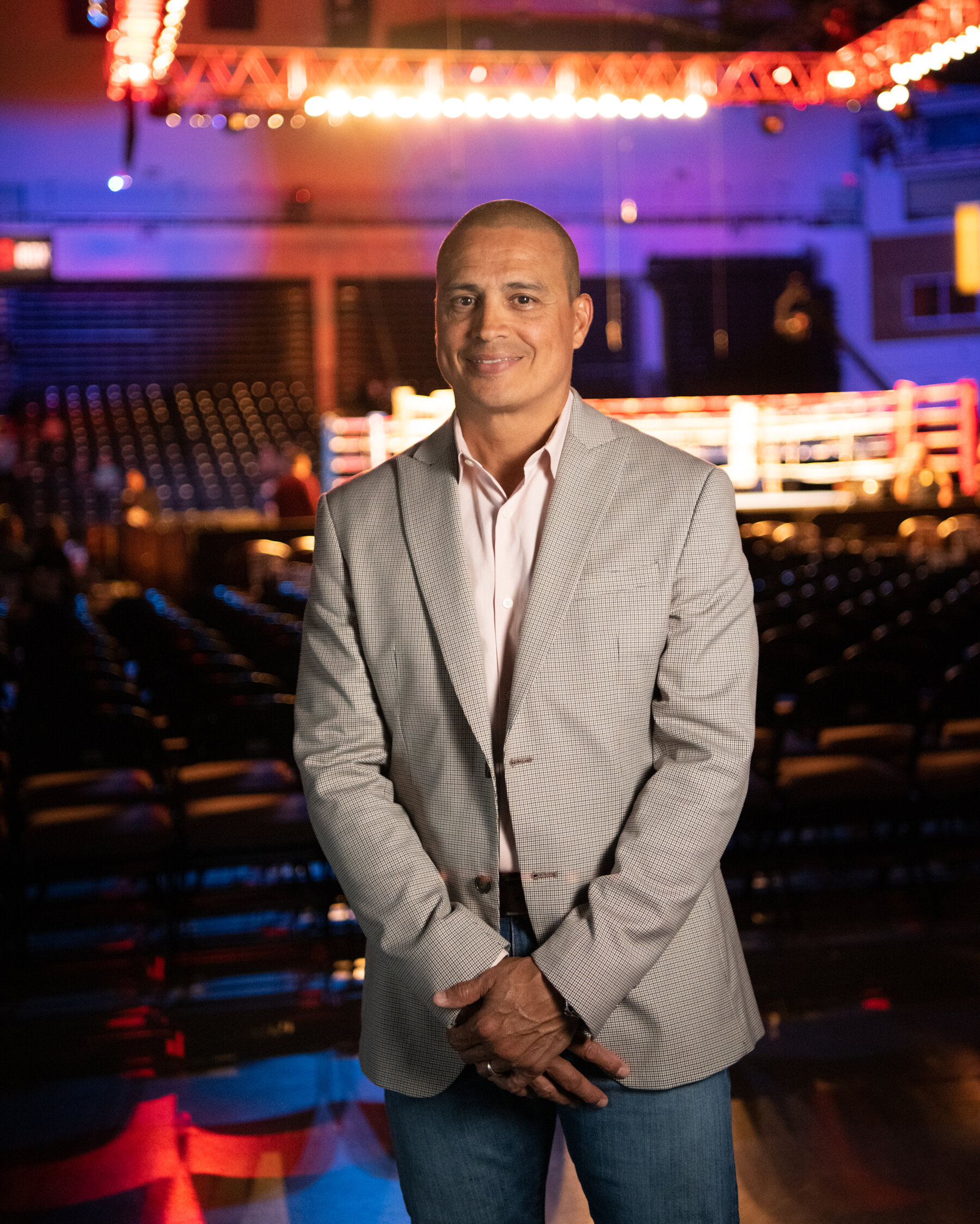 Alexis Arguello Jr., in a grey suit jacket and jeans, standing in front of a boxing ring