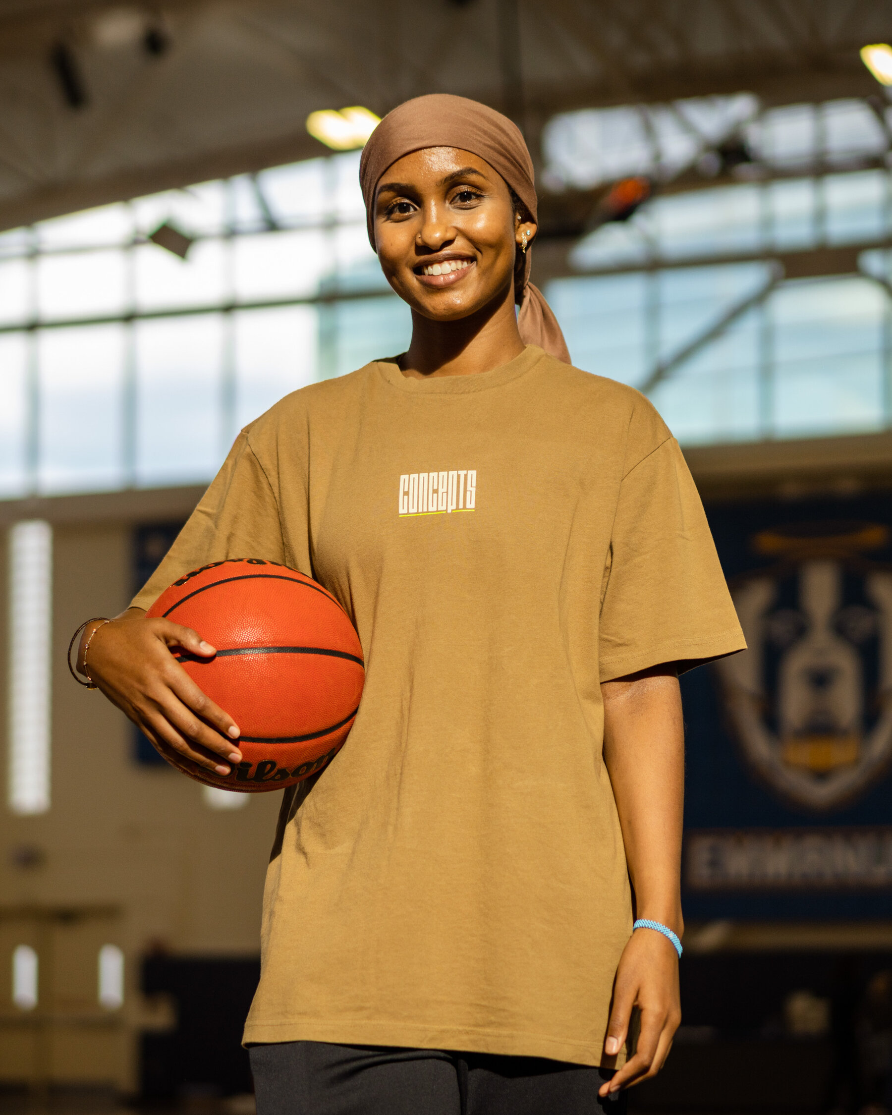 Jamad Fiin standing in a gymnasium, wearing a brown bandana, holding a basketball in one arm.