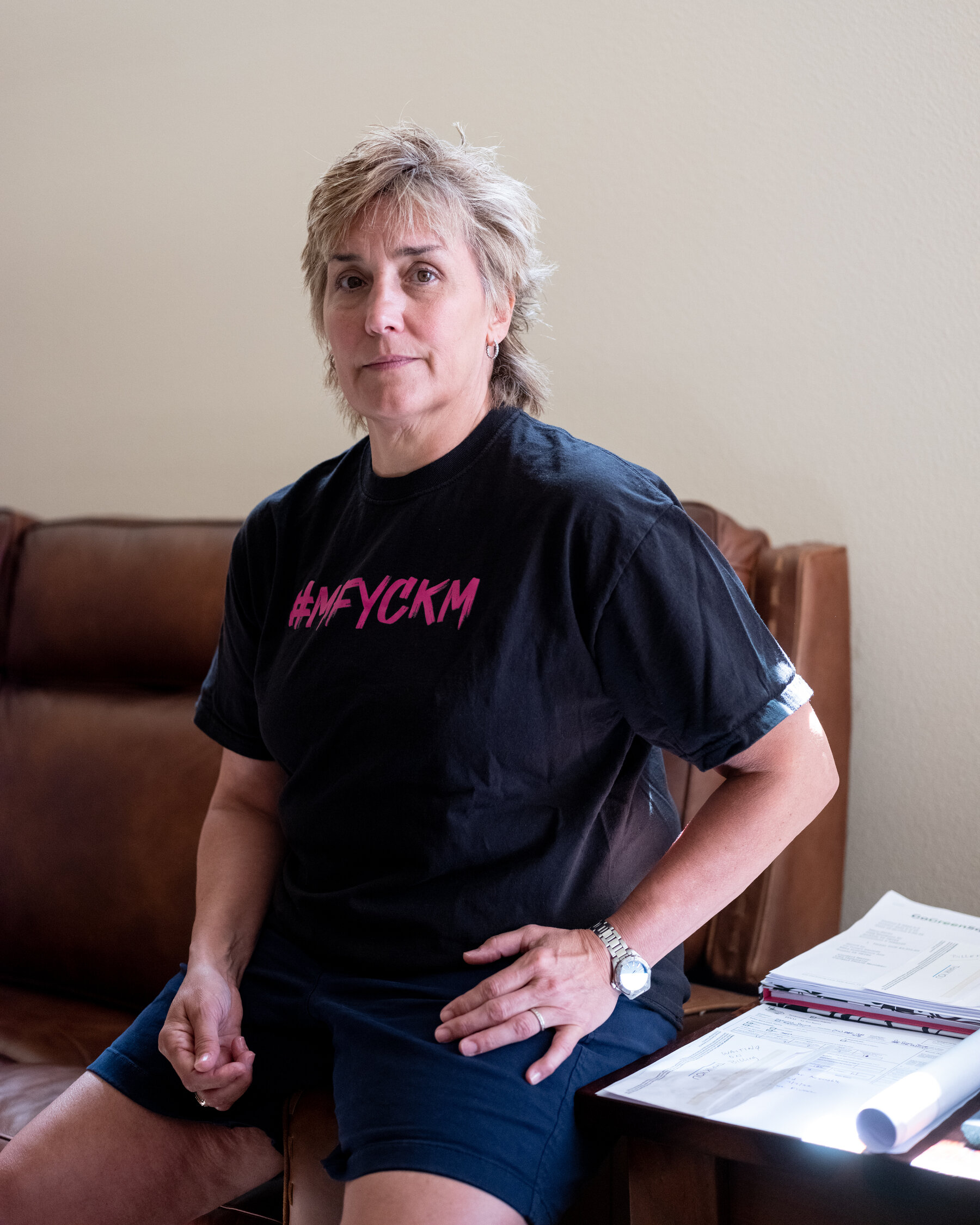 Christy Martin posing on a brown couch, wearing a black t-shirt that says in pink letters #MFYCKM