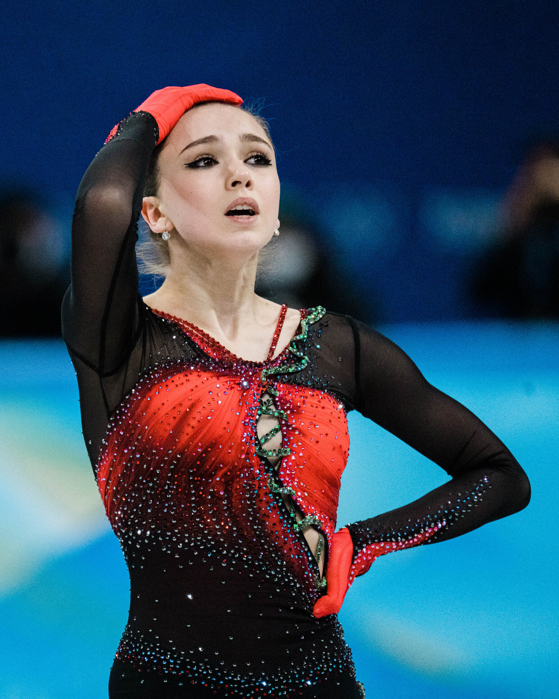 Kamila Valieva, in a black and red dress and red gloves, has a hand at her waist and another at the top of her head, after the Women’s Skating Team Free Skate.