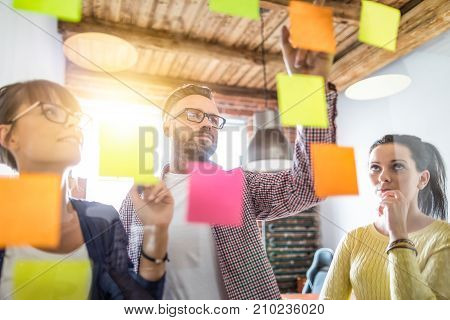 Business people meeting at office and use post it notes to share idea. Brainstorming concept. Sticky note on glass wall.