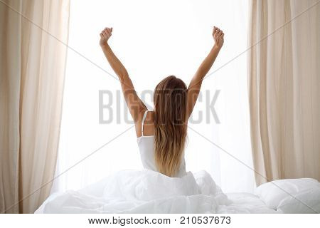 Alarm clock standing on bedside table has already rung early morning to wake up woman is stretching in bed in background. Early awakening, not getting enough sleep, oversleep concept.