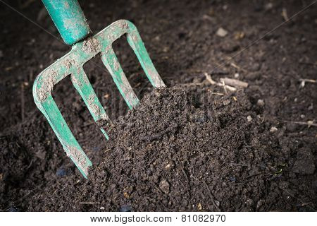 Garden fork turning  black composted soil in compost bin ready for gardening, close up.