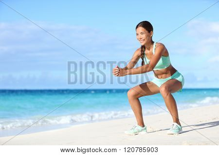 Fitness young woman working out core and glutes with bodyweight workout doing squat exercises on beach. Asian sporty girl squatting legs as part of an active and fit life.