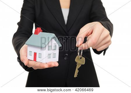 Real estate agent new house keys concept. Realtor showing holding house keys and mini house model. Buying new home conceptual image with business woman in suit isolated on white background