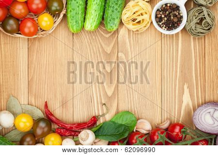 Fresh ingredients for cooking: pasta, tomato, cucumber, mushroom and spices over wooden table background with copy space