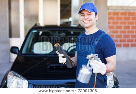 Car body repairer holding a spray gun and a sheet of sandpaper