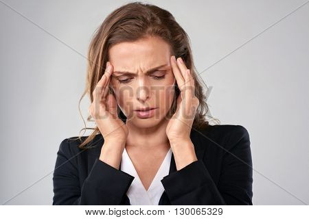 Stressful business woman massages her temple to ease her tension headache migraine head pain