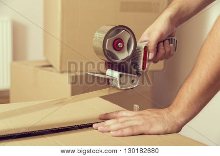 Close up of a guy's hands holding packing machine and sealing cardboard boxes with duct tape