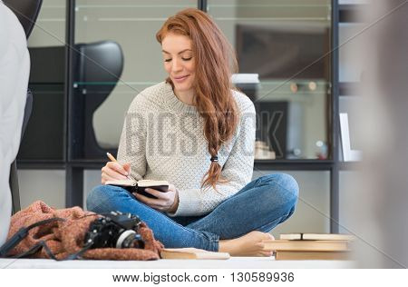 Happy young woman writing in diary. Young woman booking her dates in diary. Happy young photographer writing in her personal organizer. 