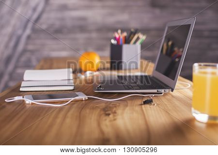 Side view of designer desktop with laptop smartphone office tools and orange. Angled laptop on table in home interior. Freelance desktop with open laptop computer