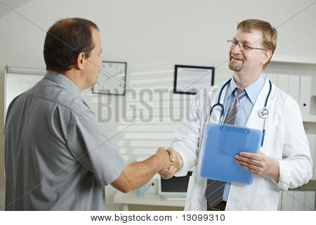 Consultorio médico - paciente de saludo doctor hombre mediana edad, estrechándole la mano.