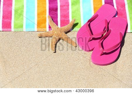 Tropical beach vacation holiday and travel concept with a colourful striped beach towel and vibrant pink sandal flip flip thongs on pristine sand with a starfish at an idyllic coastal beach resort.