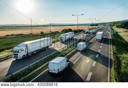 Convoy Or Caravans Of Transportation Trucks Passing Vans And Truck On A Highway On A Bright Blue Day