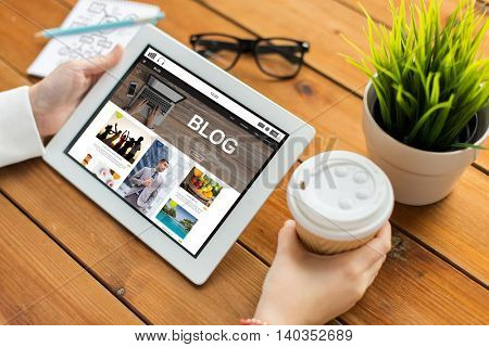 business, technology, media, internet and people concept - close up of woman with blog web page on tablet pc computer screen drinking coffee on wooden table