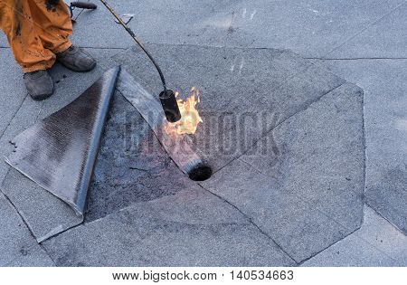 Roofer doing repair roof drain. Flat roof installation. Heating and melting bitumen roofing felt. Flat roof repairing with roofing felt. Professional master making waterproofing.