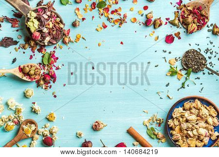 Different herbs for making healthy tea: mint, cinnamon, dried rose in bowl, camomile flowers in spoons over blue painted background, top view, copy space, horizontal composition