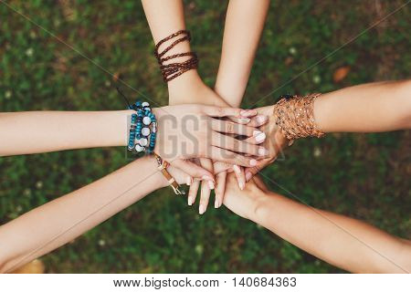 United hands of young females, top view. Stylish hands of girlfriends in boho hippie bracelets at green grass background. Togetherness and support, youth fashion and active lesiure. Women friendship