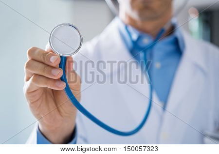 Male doctor showing stethoscope for checkup. Close up of doctor hand holding stethoscope to auscultate breath. Doctor with stethoscope in hand on hospital background for medical visit.