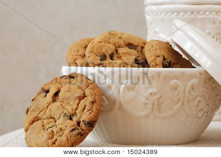 Freshly baked, chocolate chip cookies in a vintage dish with matching cookie jar in the background.  Close-up with shallow dof.