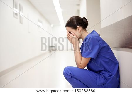 people, medicine, healthcare and sorrow concept - sad or crying female nurse at hospital corridor