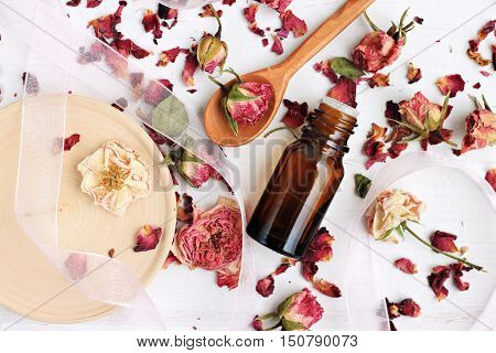 Essential rose oil, dried rose petals, aroma dropper bottle, wooden preparation utensils. Natural beauty care.