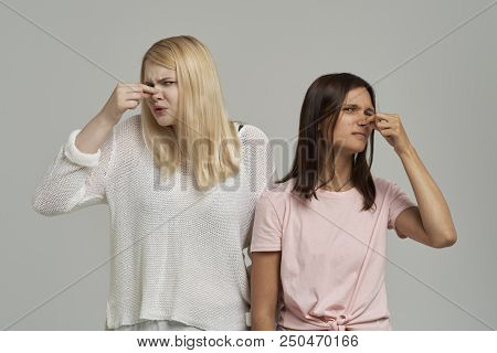 Two Frowning Women Having A Disgusting Look, Clamping Her Nose And Holding Her Breath Because Of An 