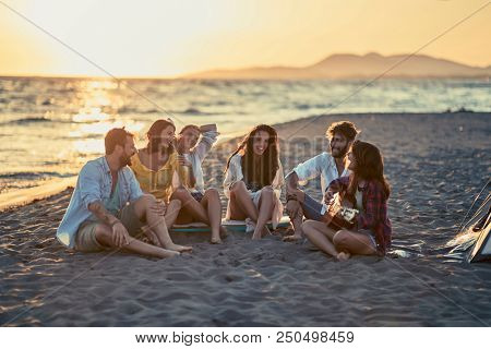 Group of smiling friends with guitar at beach. friends relaxing on sand at beach with guitar and singing
