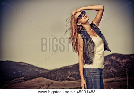 Beautiful young woman posing on a road over picturesque landscape.