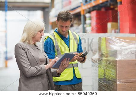 Manager using tablet while worker scanning package in warehouse