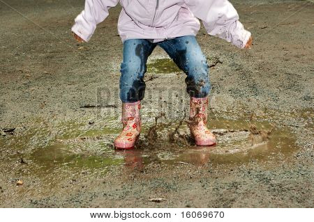 Feet of a little girl jumping into a muddy puddle