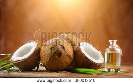 Coconut palm oil in a bottle with coconuts and green palm tree leaf on brown background. Coco nut closeup. Healthy Food, skin care concept. Vegan food. Skincare treatments. Aromatherapy.