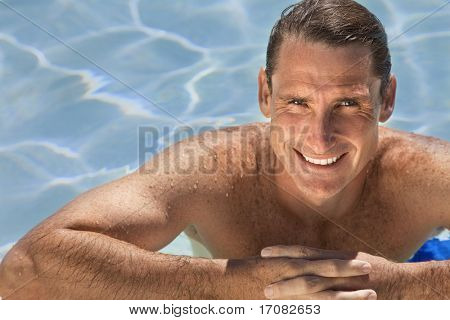 Close up portrait of a handsome and happy mid aged man relaxing resting on his hands at the side of a sun bathed swimming pool smiling with perfect teeth.